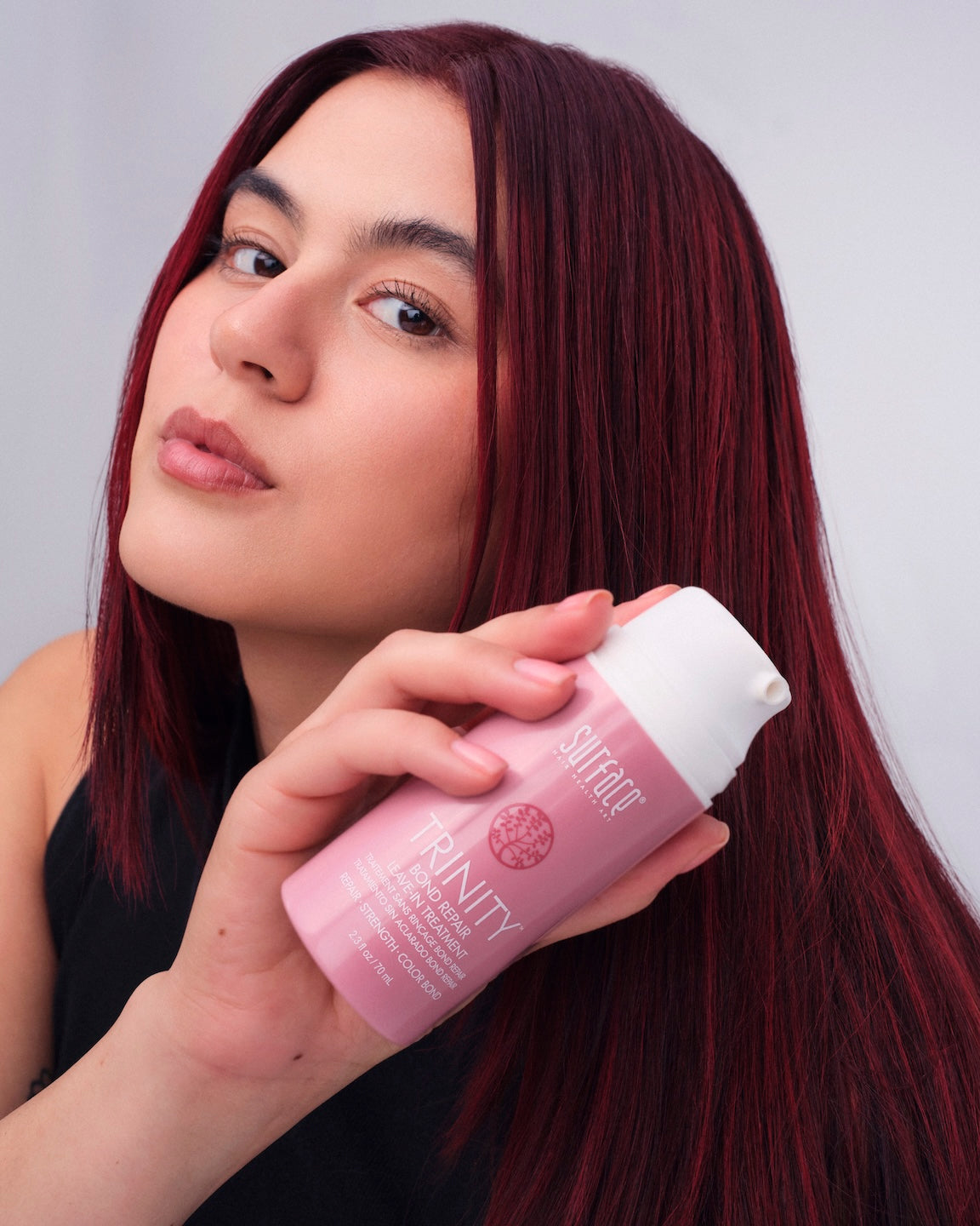Model with red color hair holding Trinity Bond Repair bottle.